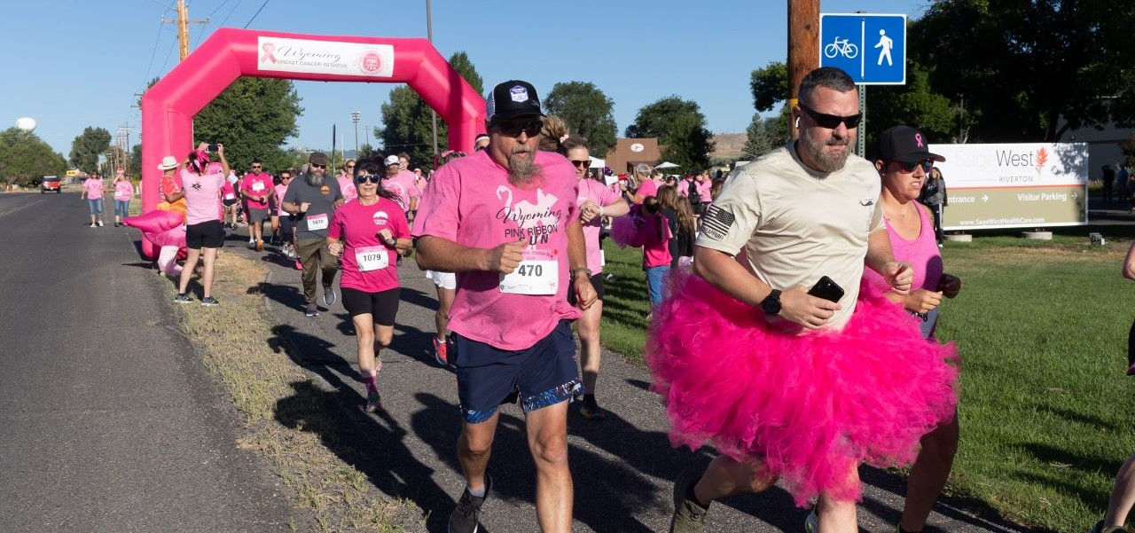 runners running through pink ribbon run starting line