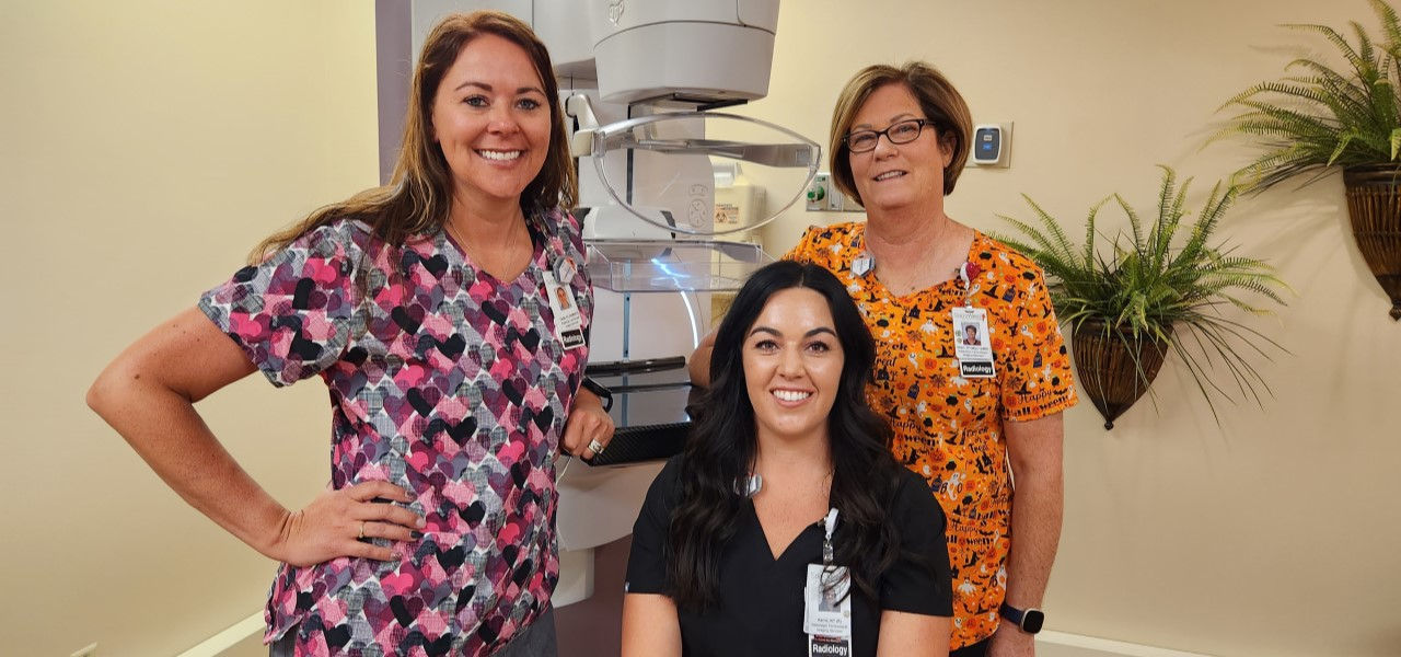 Smiling caregivers in front of mammo machine