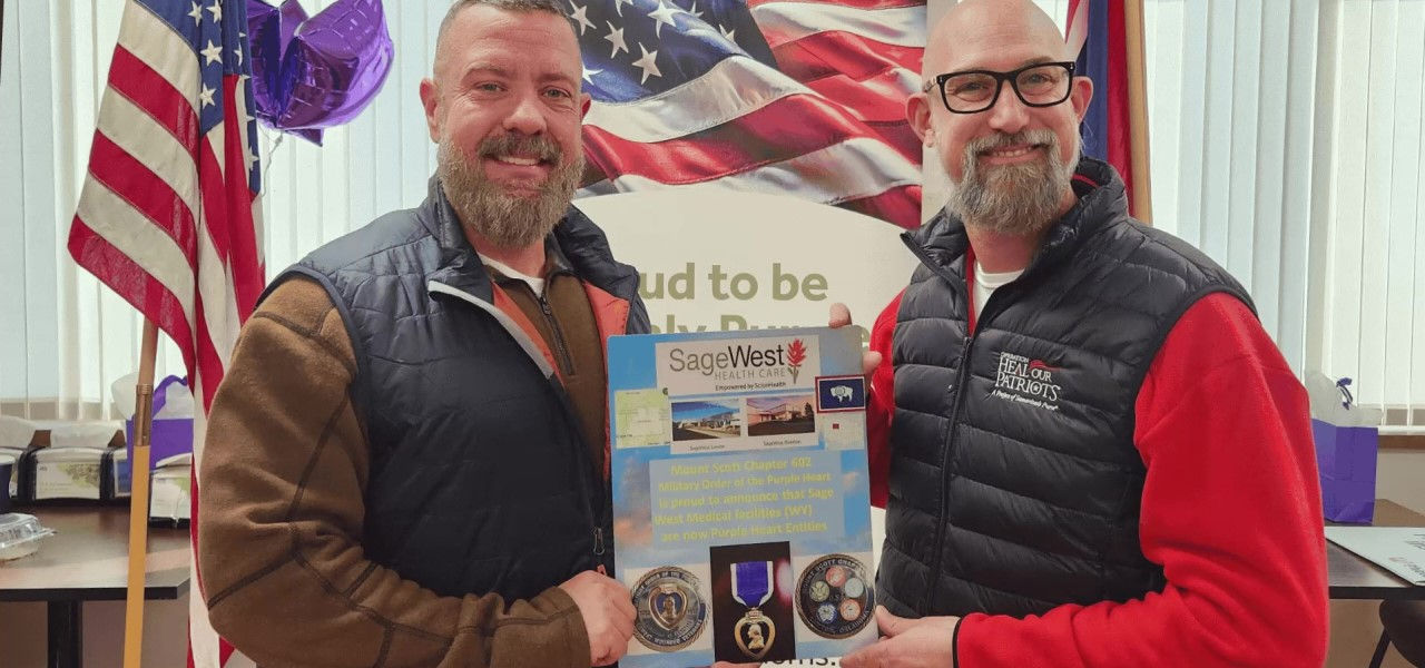 Two men smiling and holding National Purple Heart Day plaque