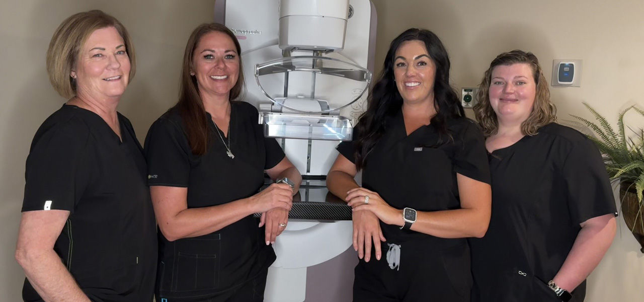 mammo team at SageWest. 4 mammogram techs pose around the mammogram machine